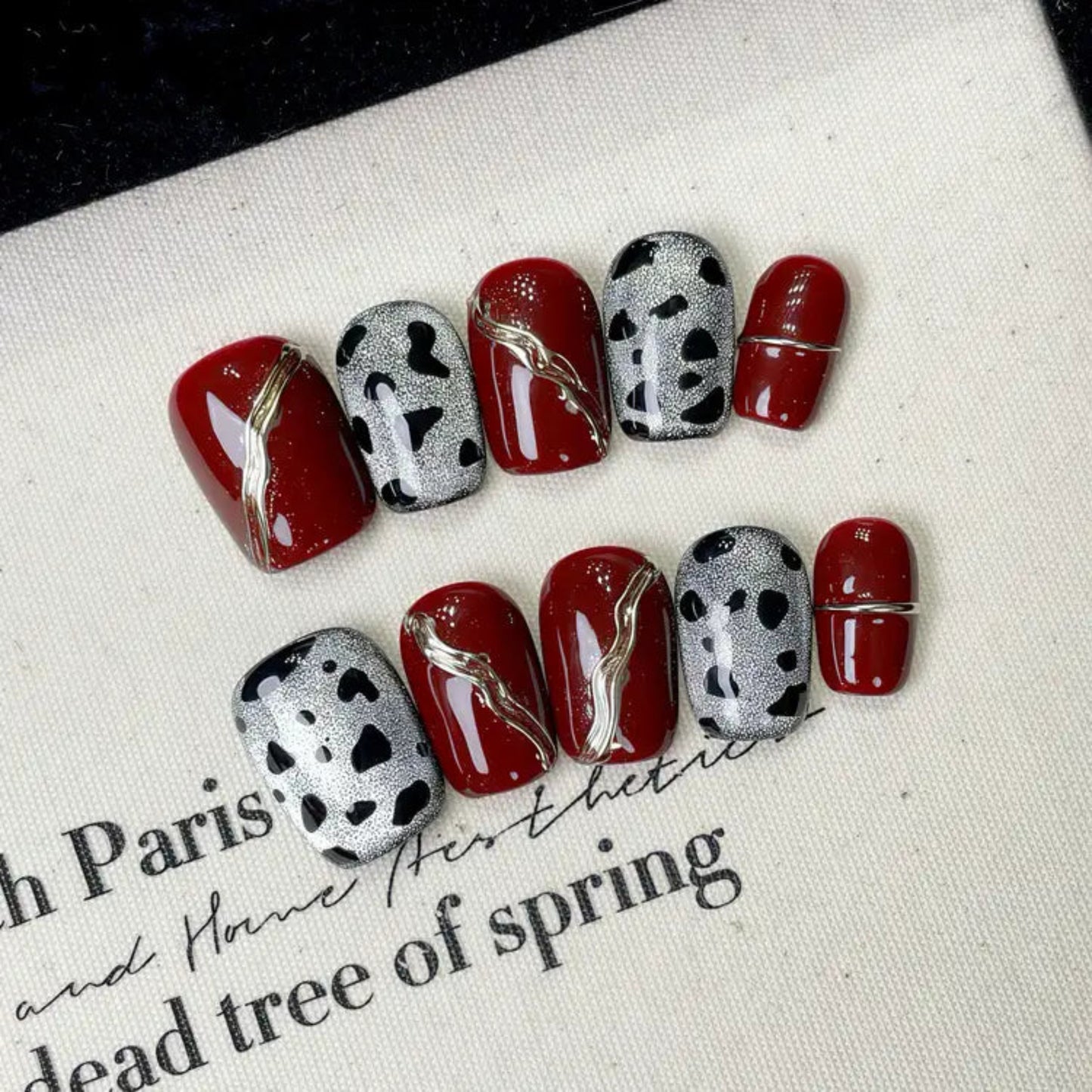Nails with red and black designs on a white surface with text