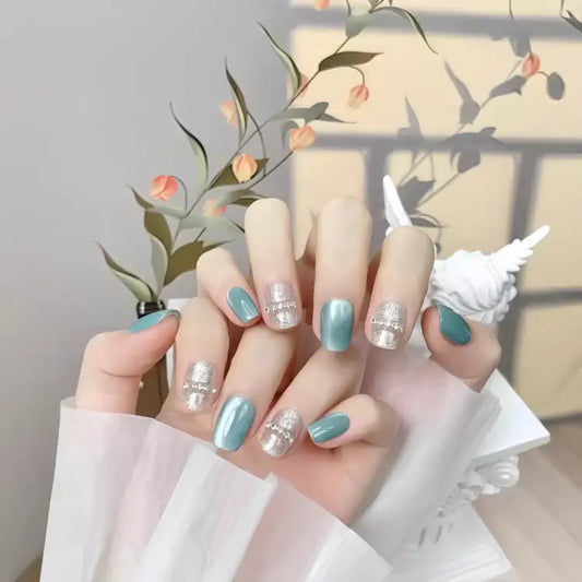 Hand with turquoise and silver nail polish holding a white shell against a decorative background