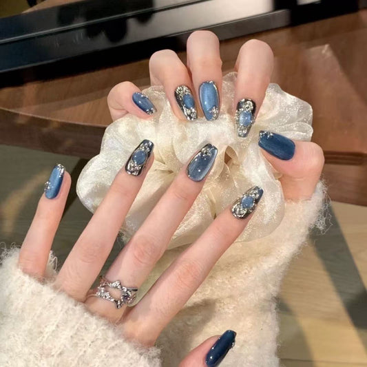 Hand with blue nail polish and decorative elements holding a white textured object.