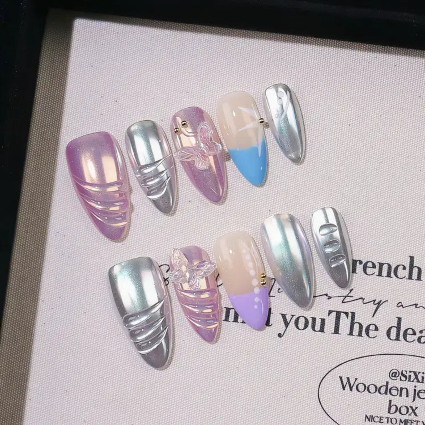 Set of multicolored nail art designs on a textured surface with text.