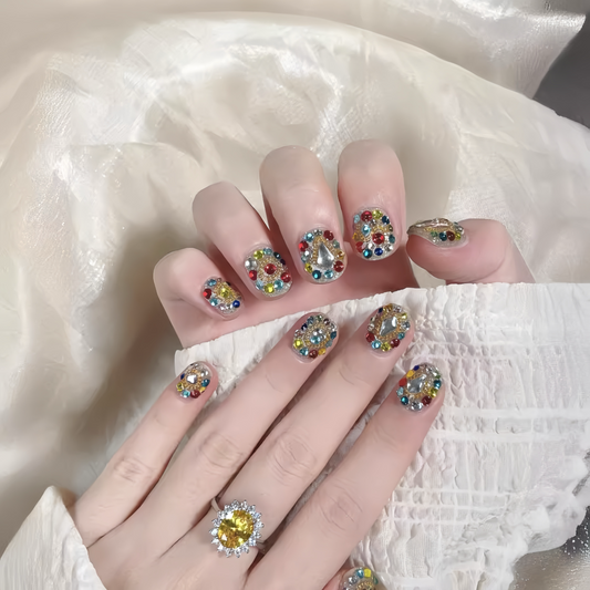 Close-up of a hand with multicolored gemstone nail art on a white fabric background