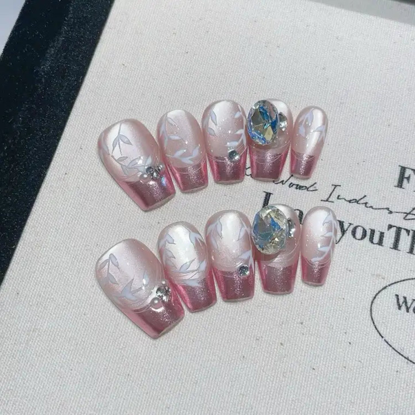 Set of decorative false nails with pink and white design on a textured surface.
