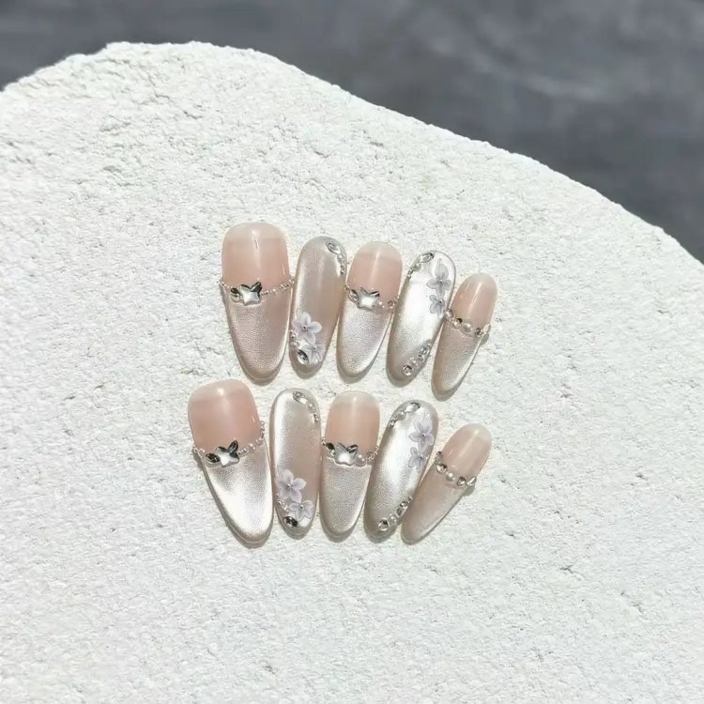 Set of decorative false nails with heart and bow designs on a textured white surface.