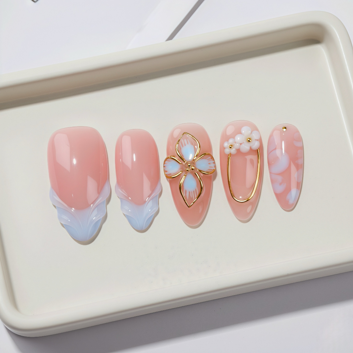 Set of pink and gold nail art designs on a white tray