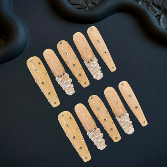 Set of beige false nails with pearls and rhinestones on a dark surface
