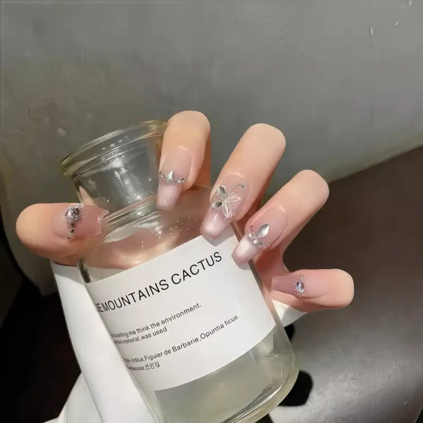 Hand holding a small glass jar labeled 'Mountains Cactus' with decorative nails.