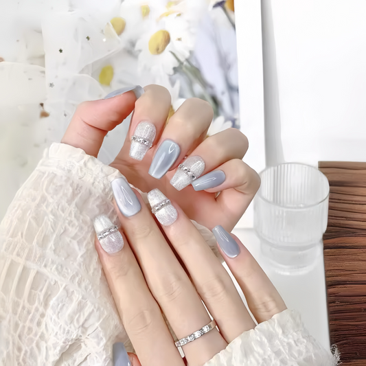 Hand with light gray and white nail polish with decorative elements, wearing a white lace garment.