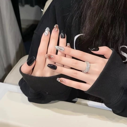 Close-up of hands with black nail polish and silver rings, wearing a black sweater.