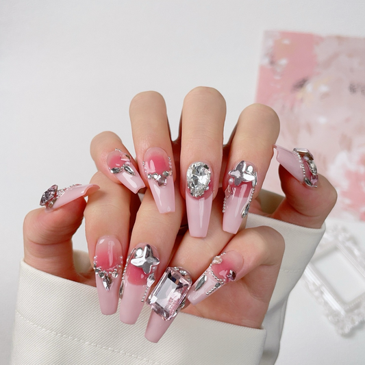 Hand with pink nails featuring silver gemstone decorations on a light background