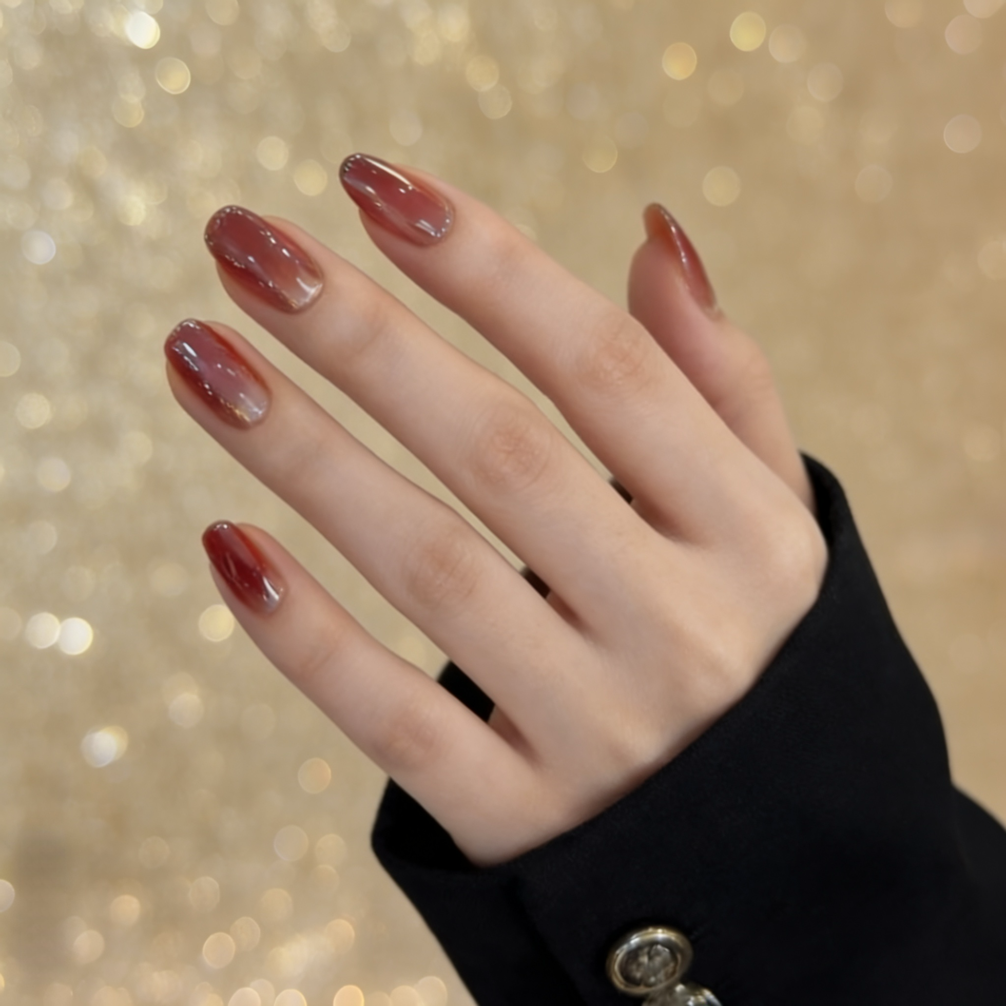 Hand with brown nail polish against a blurred gold background