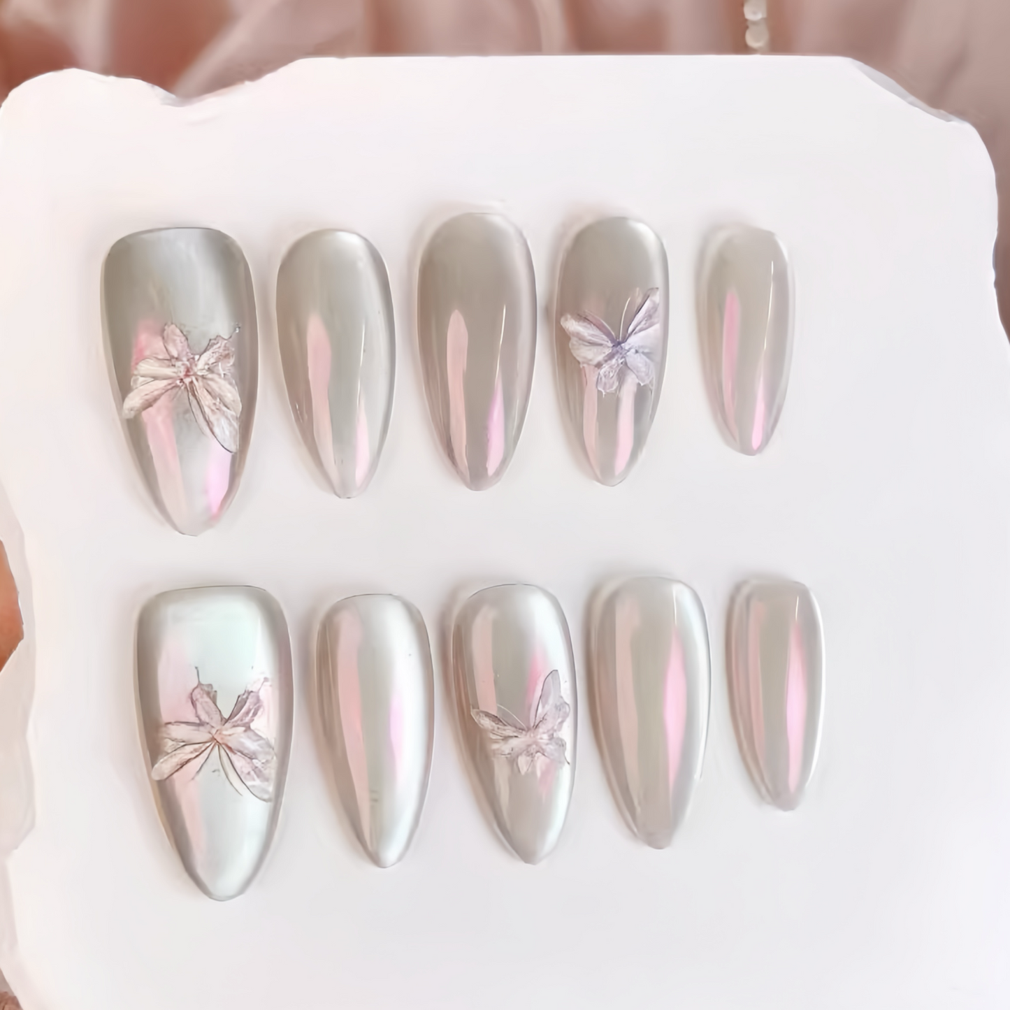 Set of silver and pink butterfly nail art designs on a white tray.