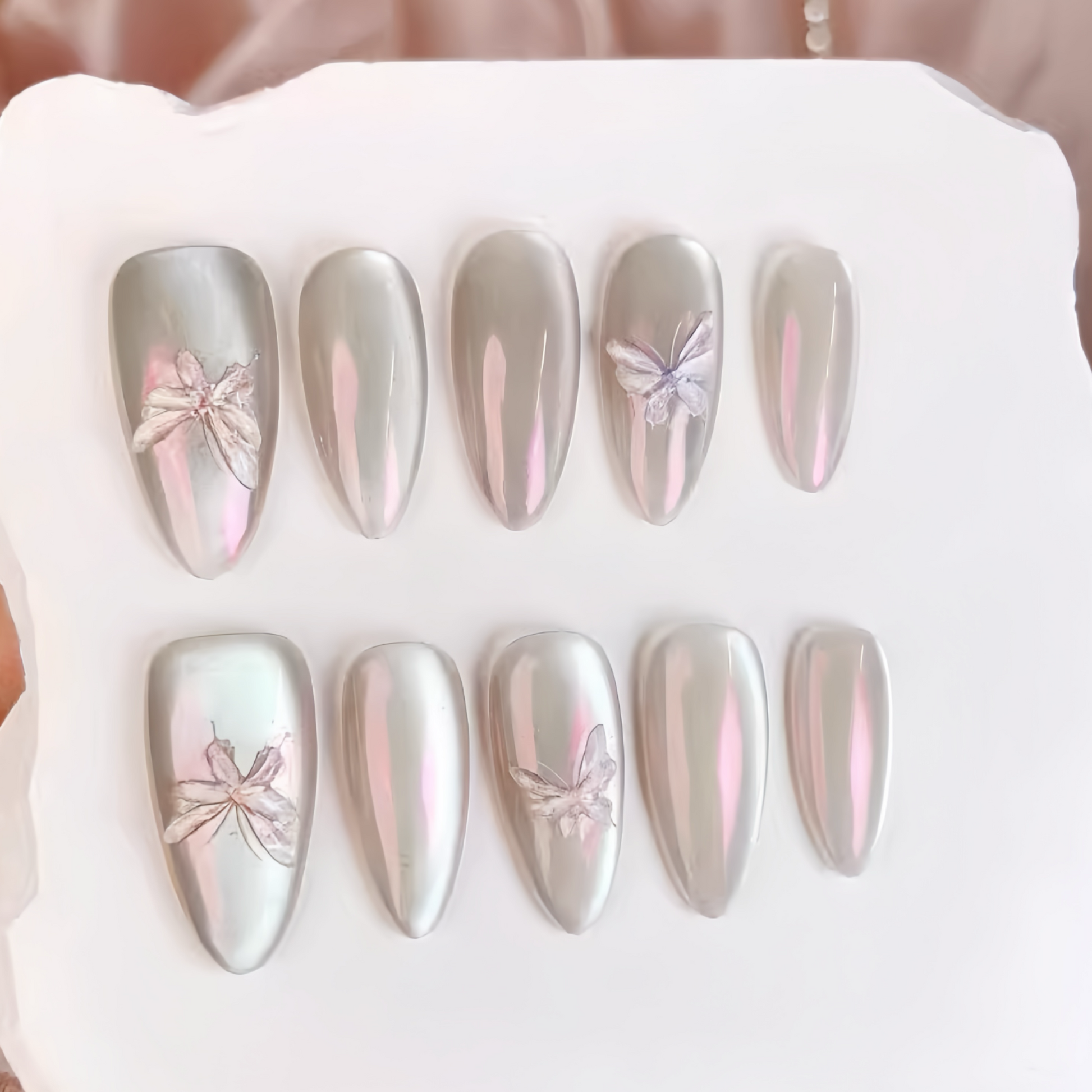 Set of silver and pink butterfly nail art designs on a white tray.
