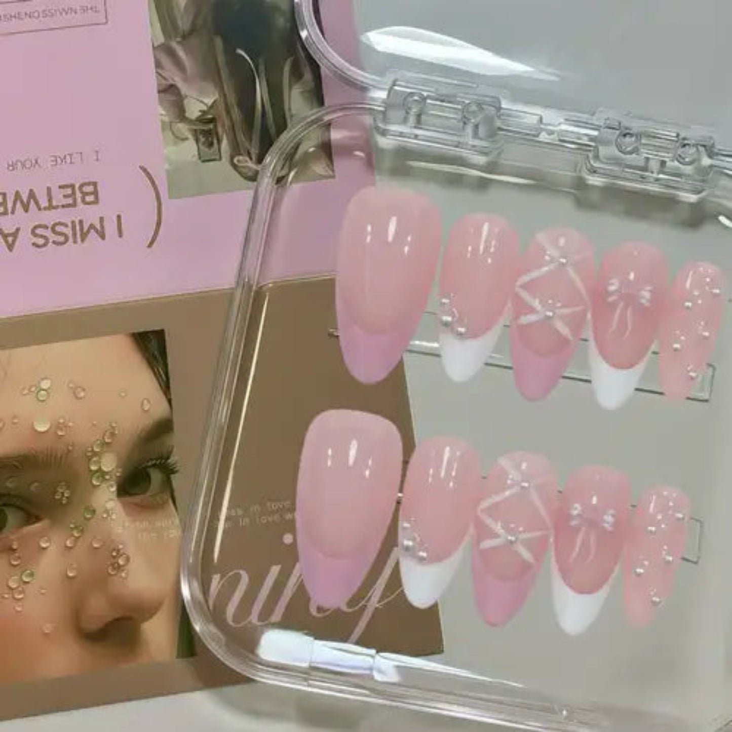 Set of pink and white press-on nails in a clear case with a blurred background.