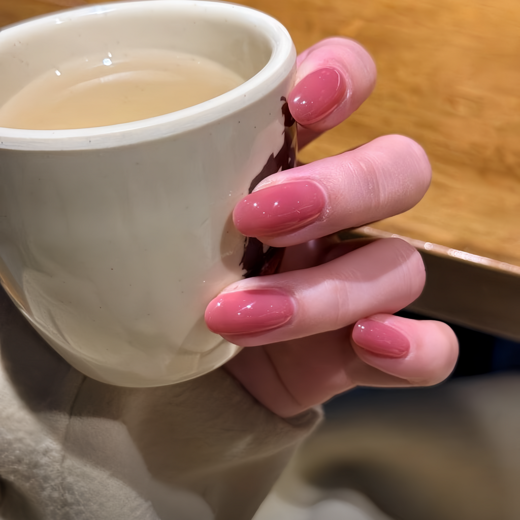 Hand with pink nail polish holding a white mug of tea on a wooden surface