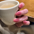 Hand with pink nail polish holding a white mug of tea on a wooden surface