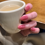 Hand with pink nail polish holding a white mug of tea on a wooden surface