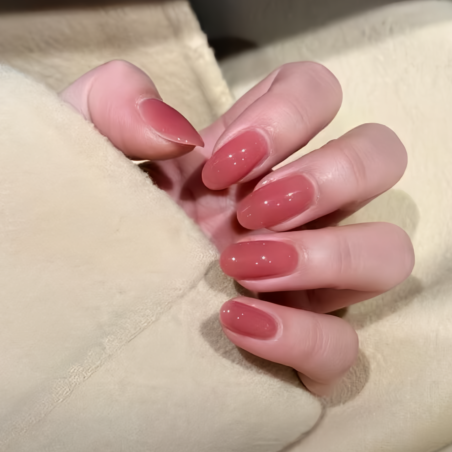 Close-up of a hand with pink nail polish on a beige background