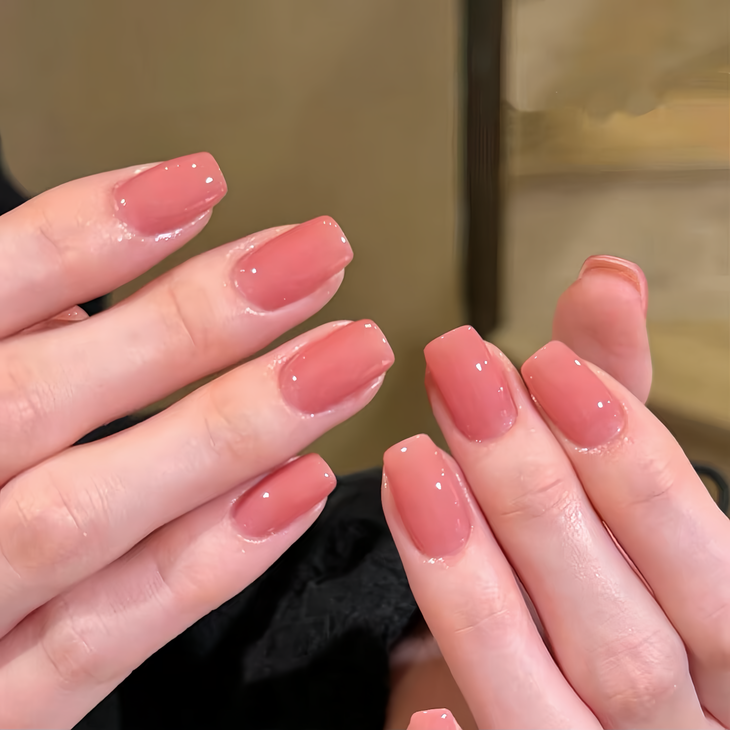 Close-up of hands with pink nail polish against a neutral background