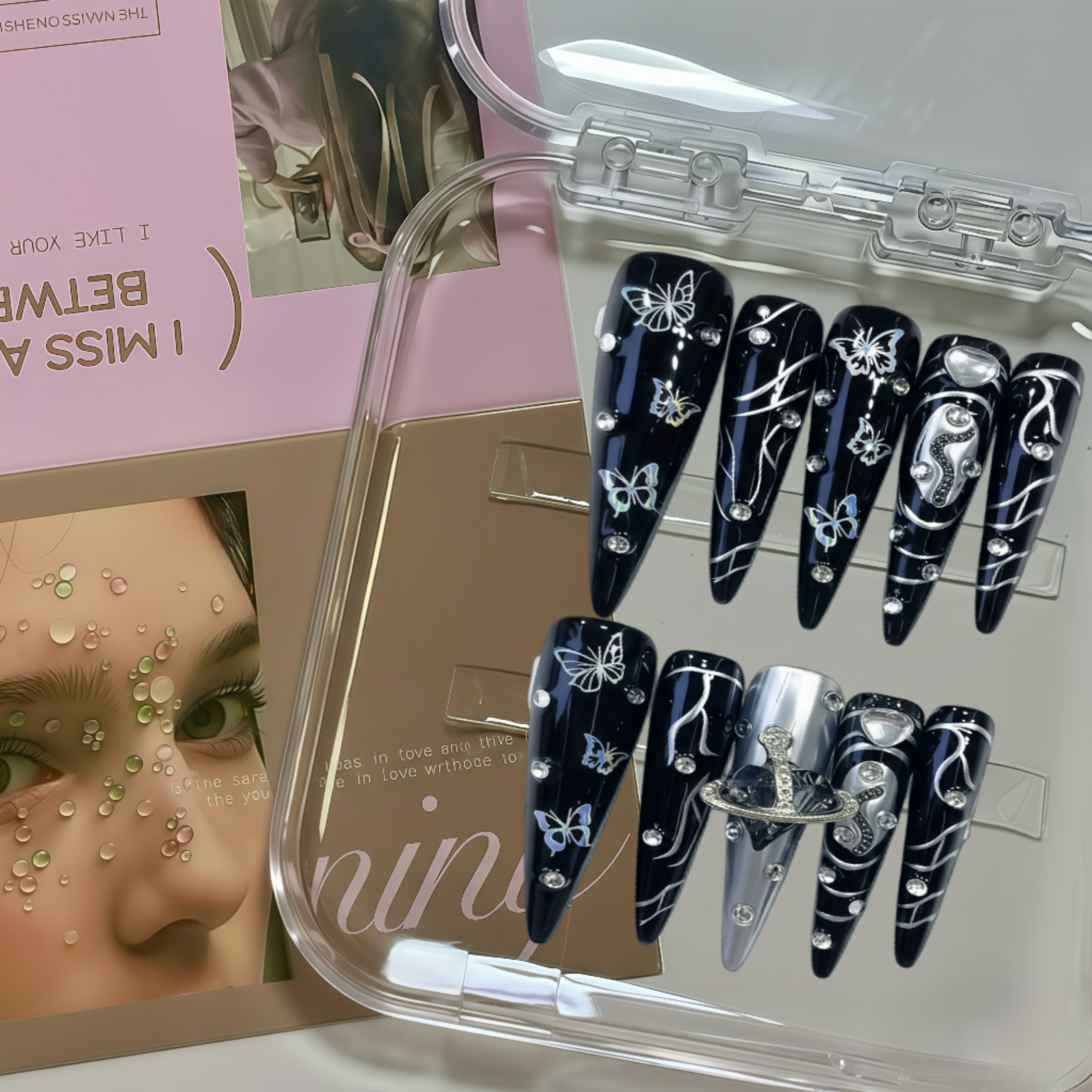 Set of black nail art designs with white decorations in a clear case, with a magazine in the background.