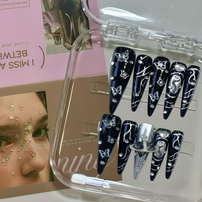 Set of black nail art designs with white decorations in a clear case, with a magazine in the background.