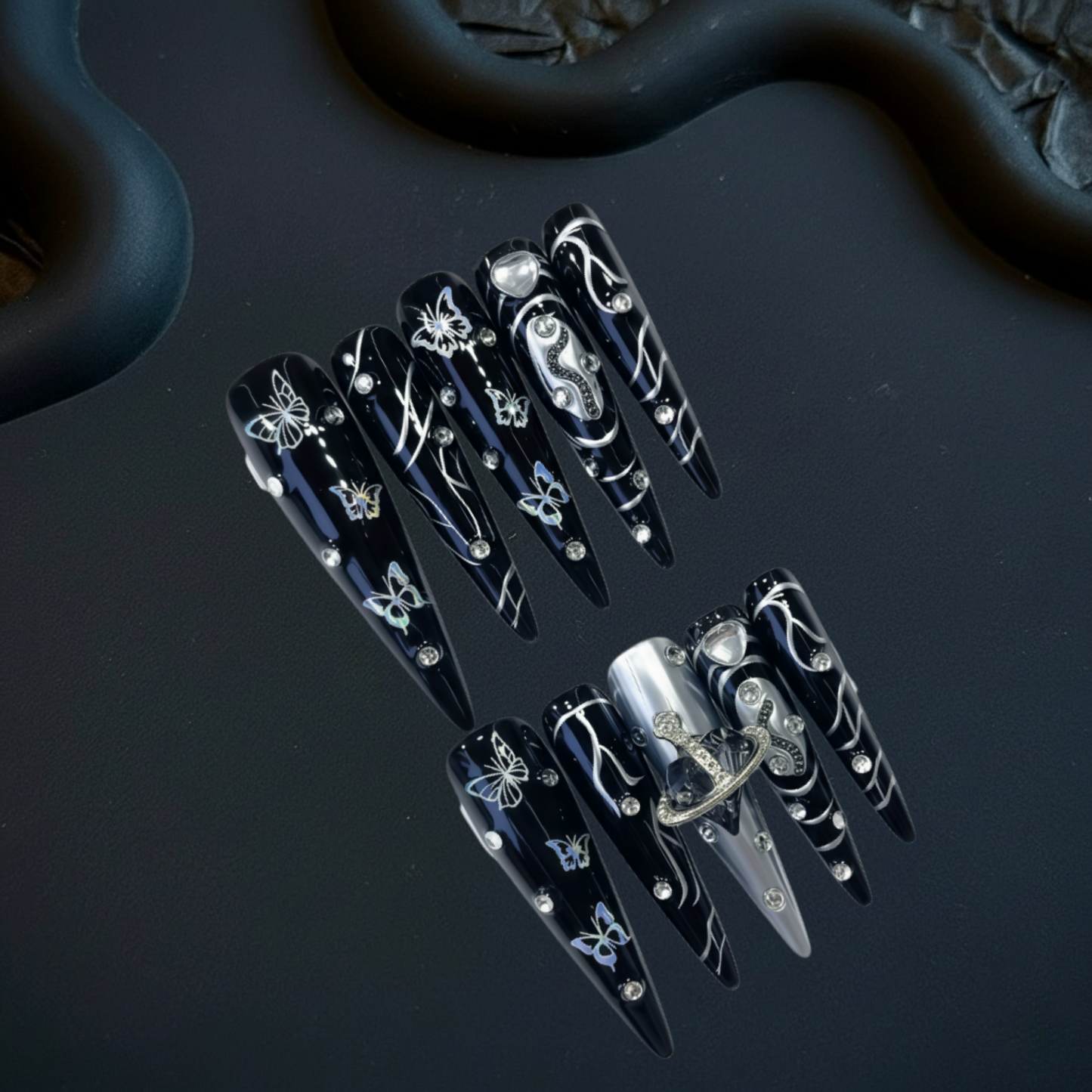 Black nail art designs with silver accents on a dark surface