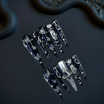 Black nail art designs with silver accents on a dark surface