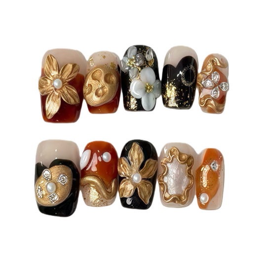 Decorative nail art with gold, black, and white designs on a white background