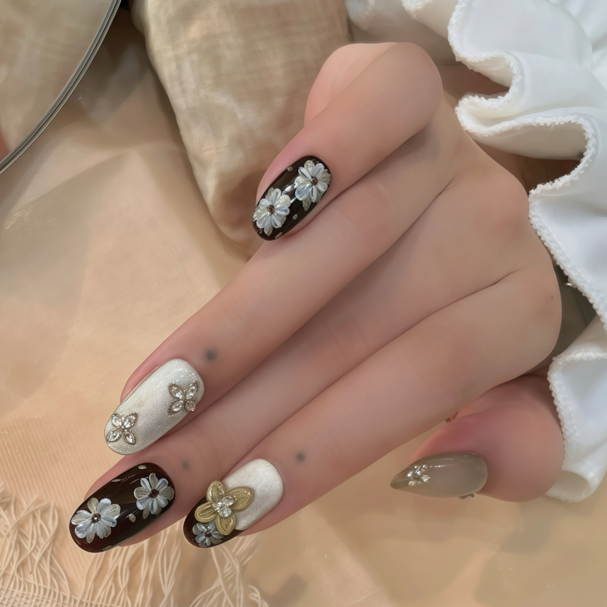 Hand with decorative nails featuring flowers and gold accents on a neutral background