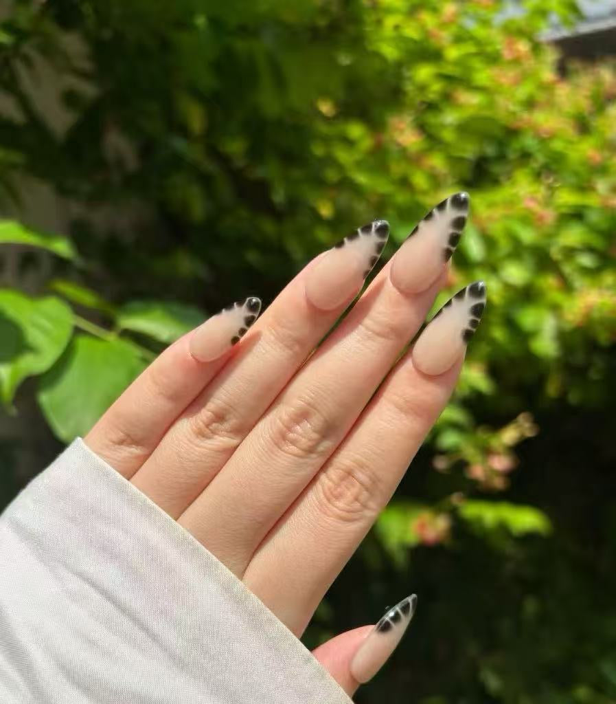 Hand with black and white nail design against a blurred green outdoor background