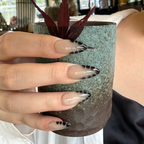 Hand with decorative nails holding a textured ceramic pot
