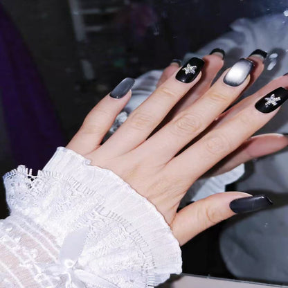 Hand with black nail polish and star decorations, wearing a white lace sleeve.