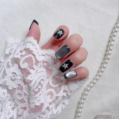 Hand with gray and black nail polish wearing a white lace glove on a light background