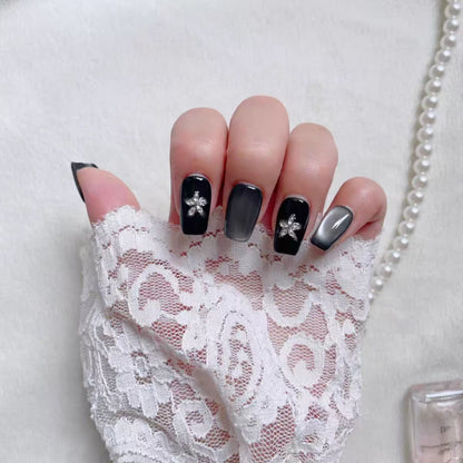 Hand with black nail art featuring flowers, wearing a white lace glove on a light background.