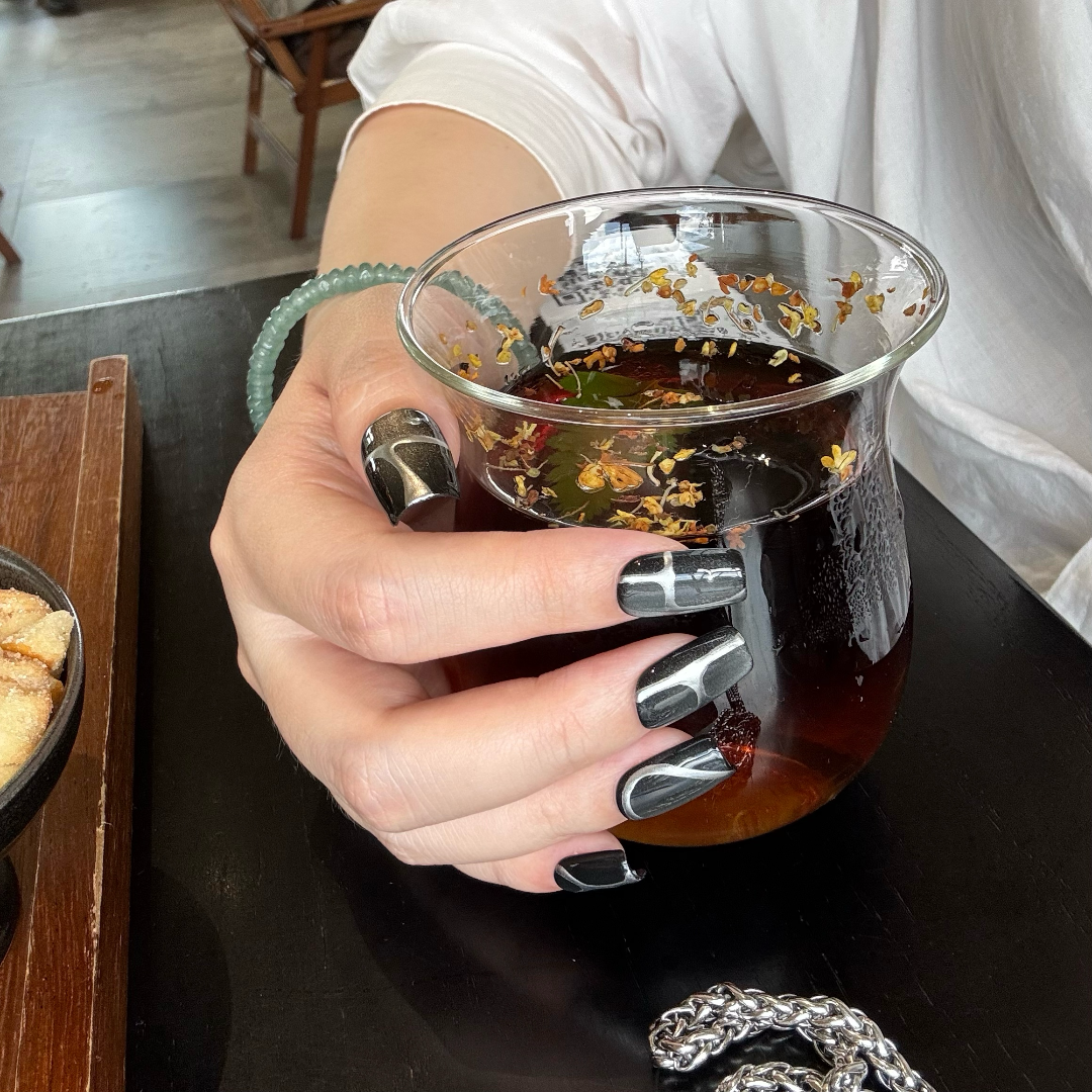 Hand holding a glass of iced tea with visible tea leaves, indoors.