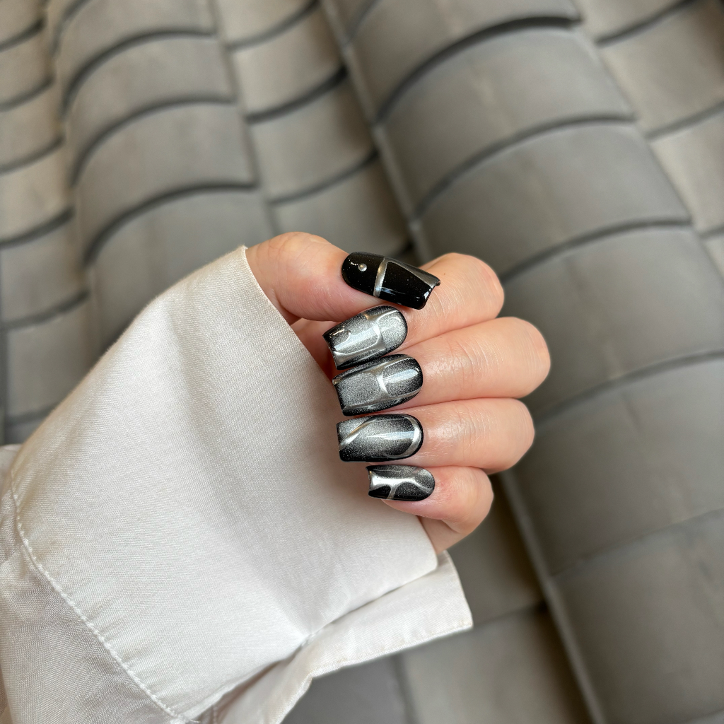 Hand with black and silver nail polish against a striped background