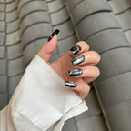 Hand with black and silver nail design against a neutral background