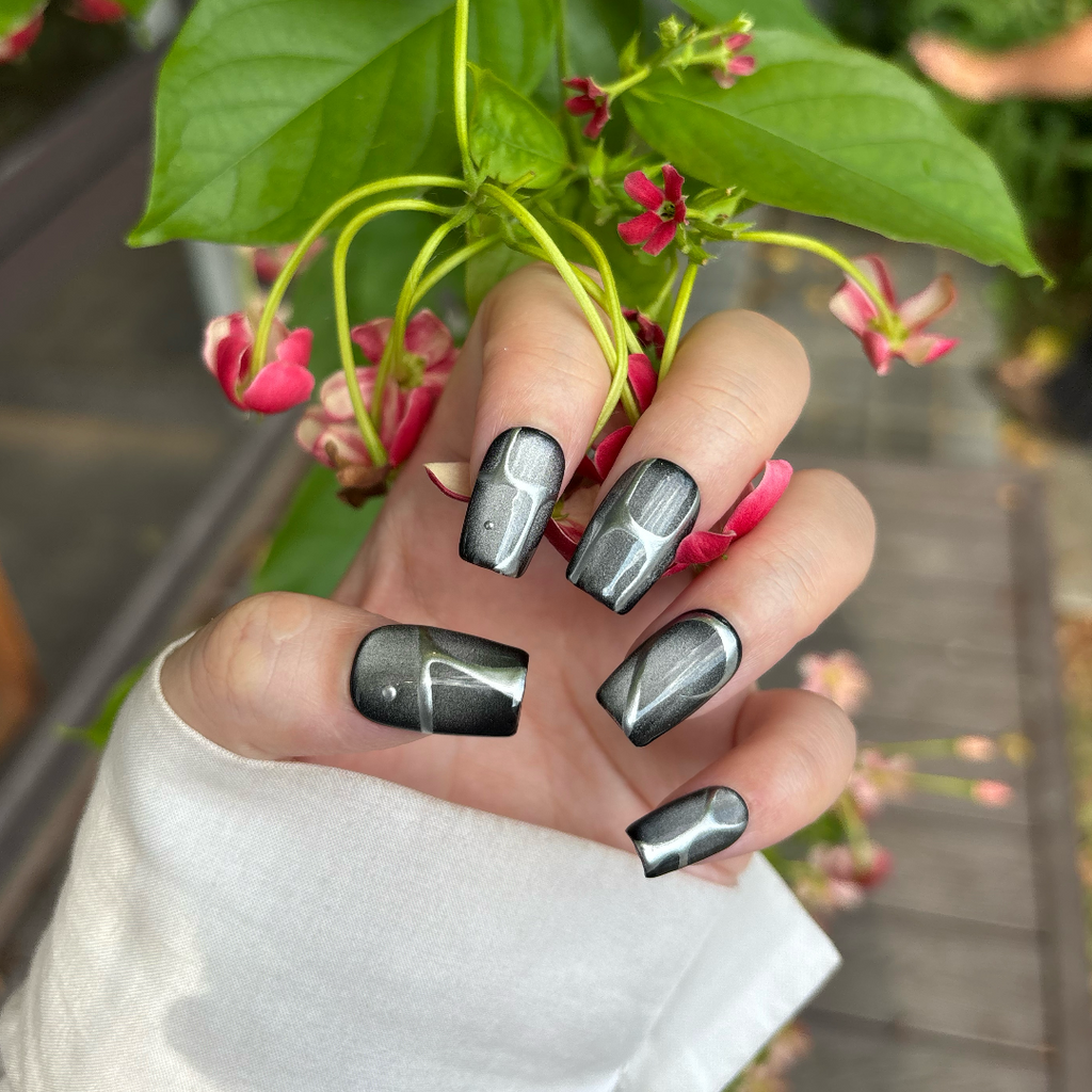 Hand with metallic gray nail polish holding a plant with pink flowers.