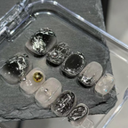 Set of silver and gold nail art designs on a gray stone surface