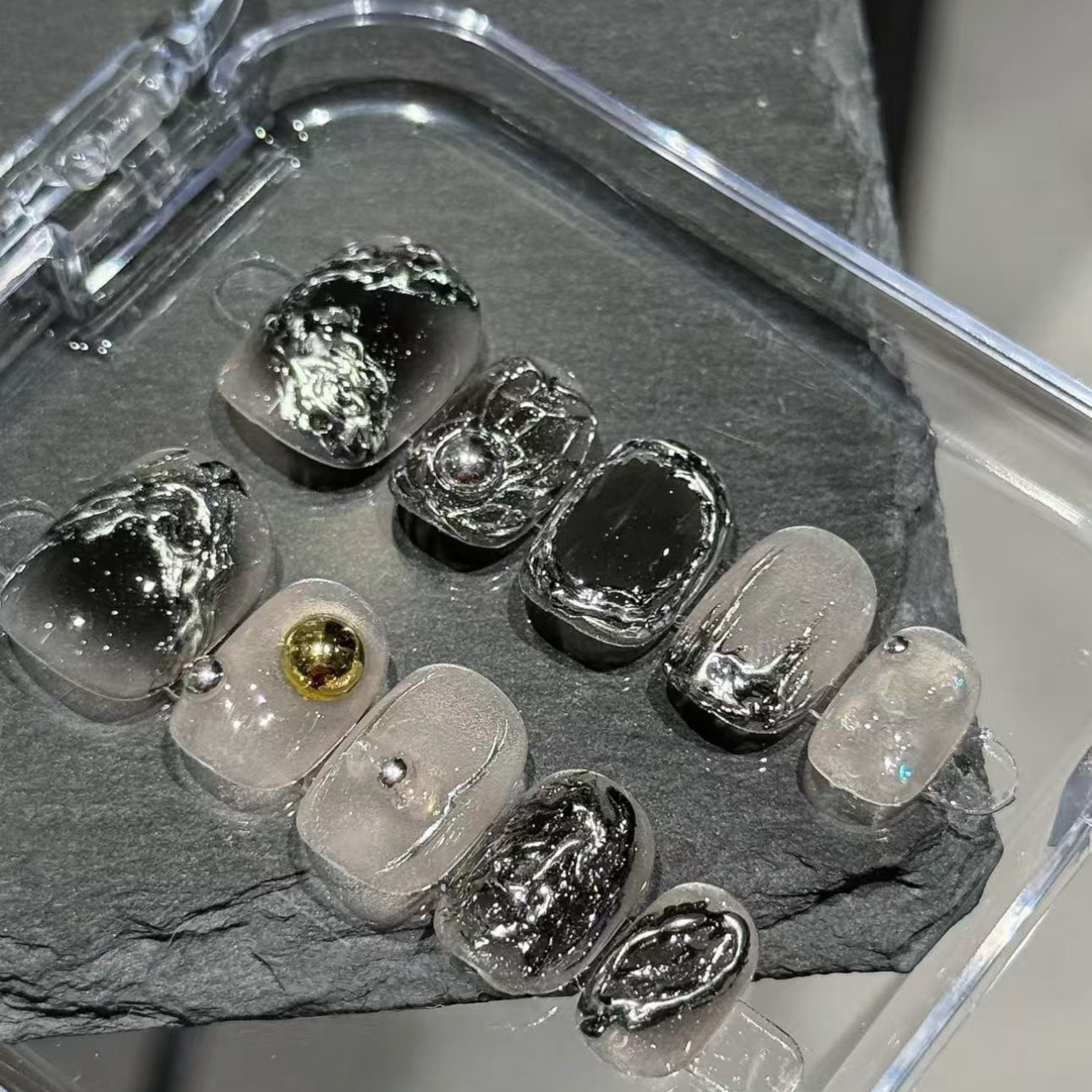 Set of silver and gold nail art designs on a gray stone surface