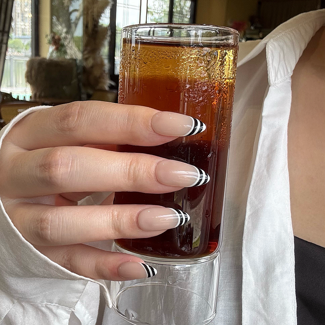 Hand with striped nail design holding a textured object against a blurred background