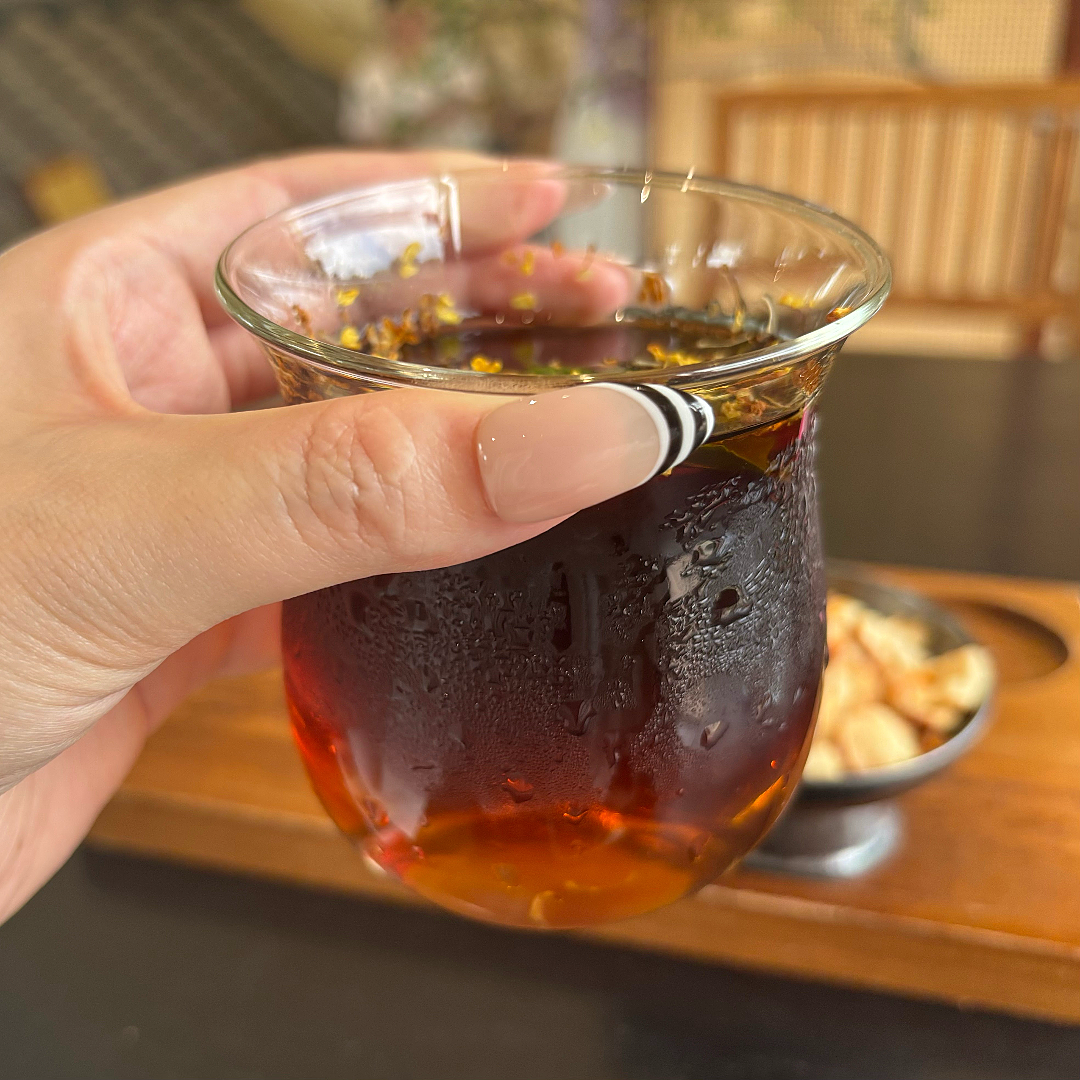 Hand holding a glass of amber-colored liquid with a blurred background
