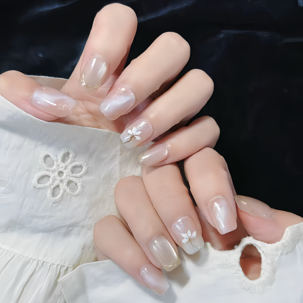 Close-up of hands with nude nail polish and subtle floral designs on a white lace fabric background.