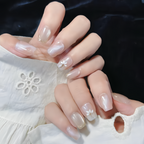 Close-up of hands with nude nail polish and subtle floral designs on a white lace fabric background.
