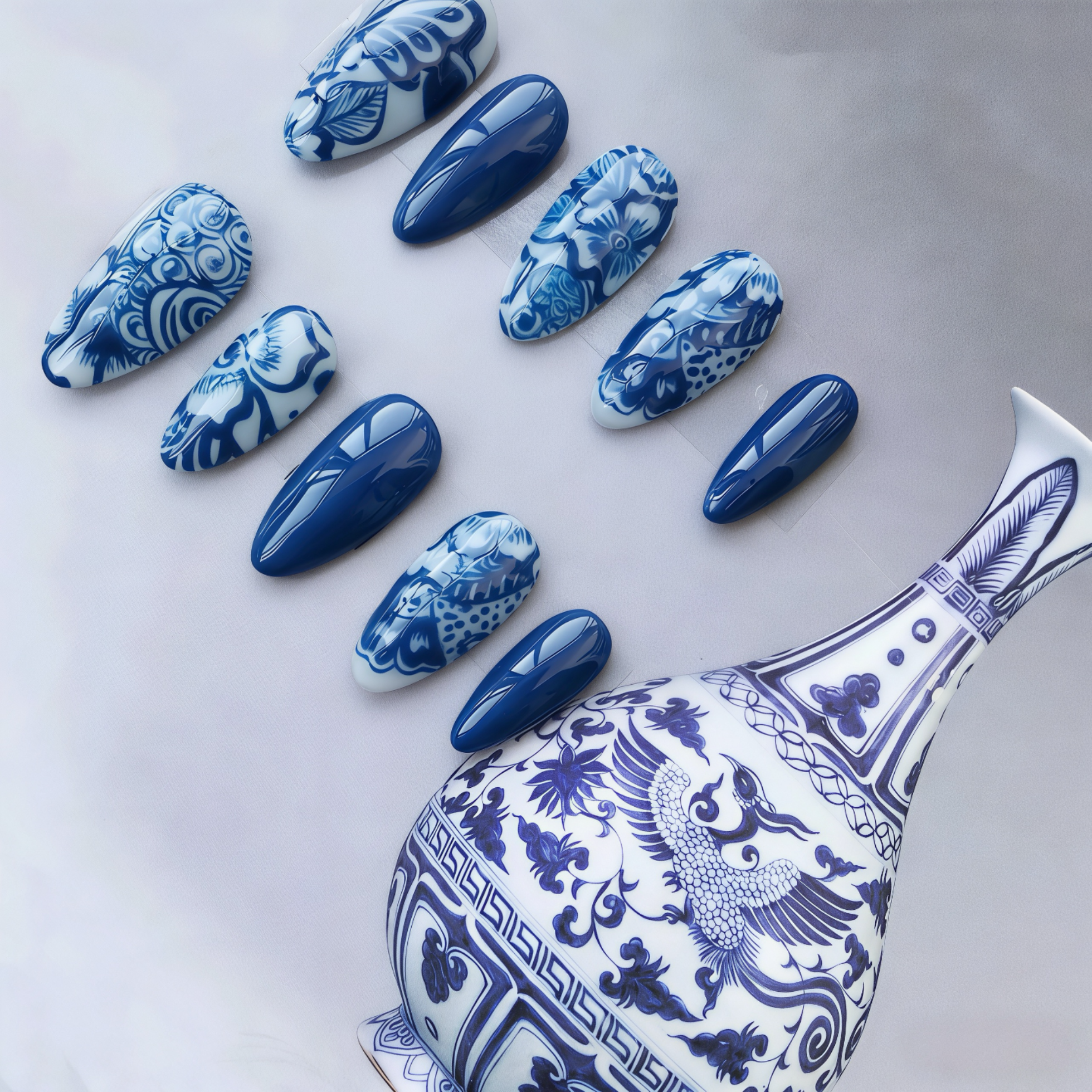 Blue and white nail art designs inspired by a ceramic vase on a light gray background