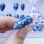 Nail art design inspired by blue and white porcelain with a blurred background of similar patterns.