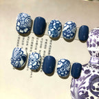 Nails with blue and white floral patterns on a textured surface with text.