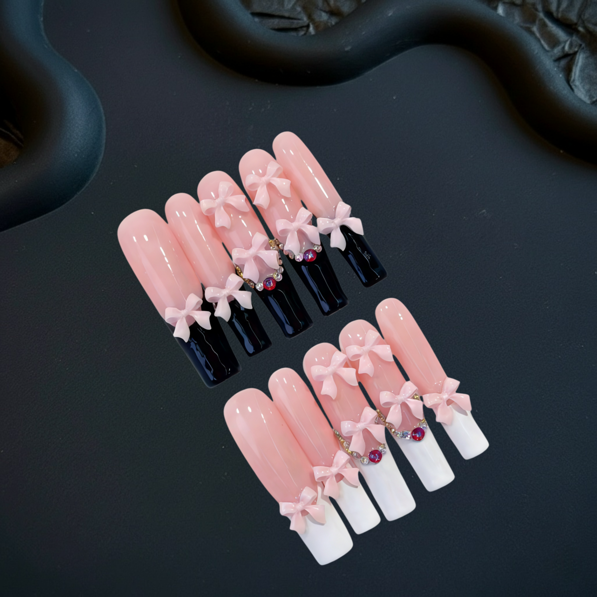 Set of false nails with pink and white tips and black and white bases on a dark surface.