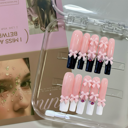 Set of decorative false nails with bows and gemstones in a clear case, with a magazine in the background.