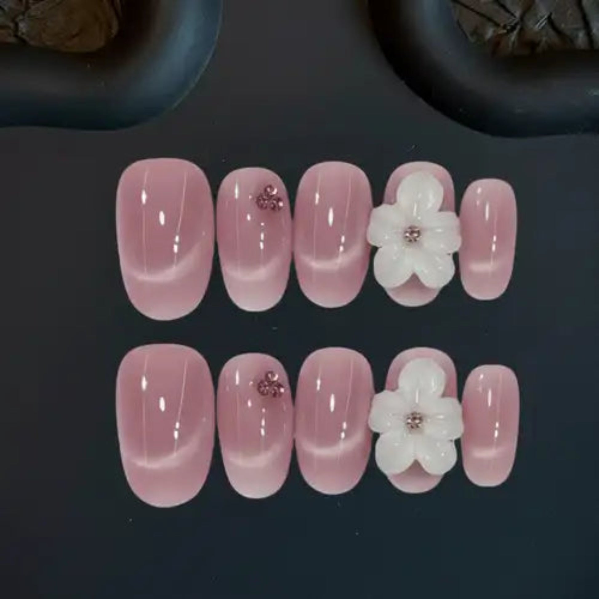 Set of pink nail art with white flowers and rhinestones on a dark background