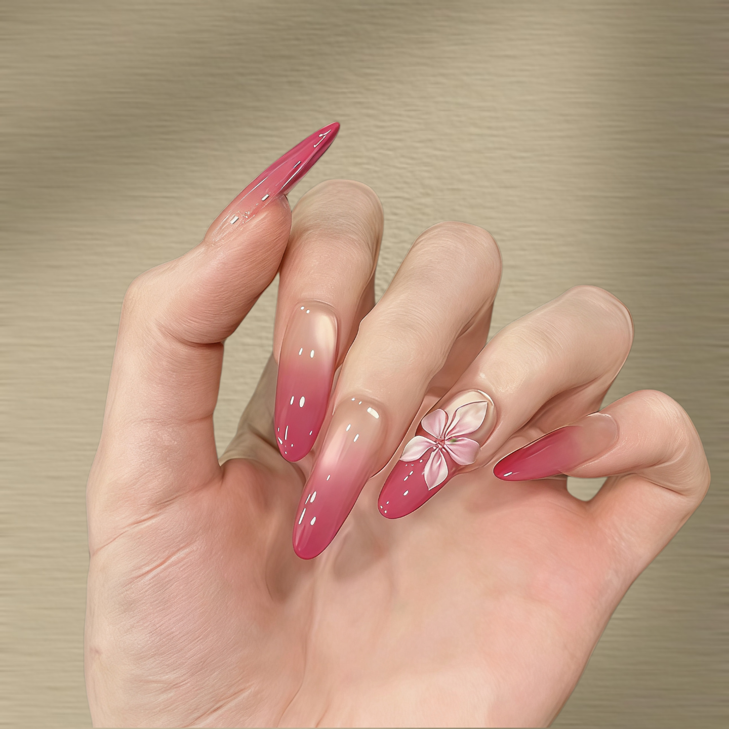 Hand with pink gradient nails featuring a floral design on a beige background